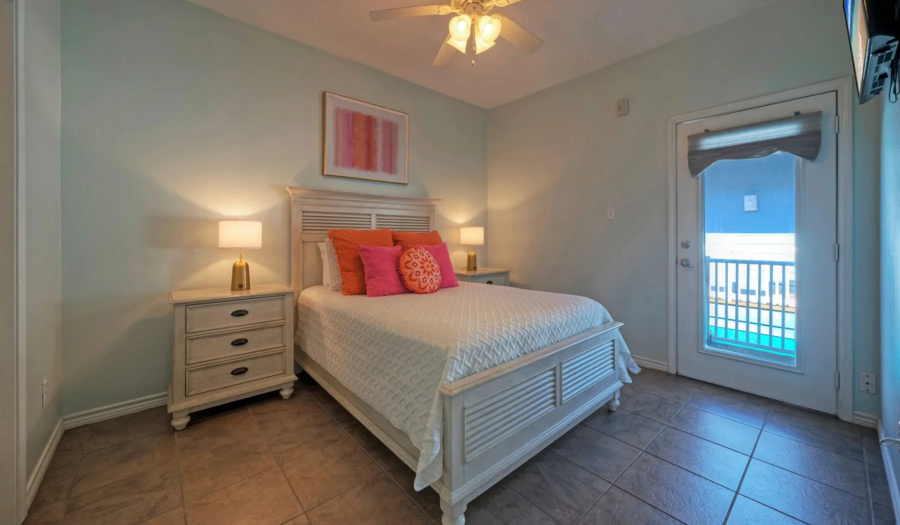 A bedroom with a neatly made bed and a glass door opening onto a balcony.