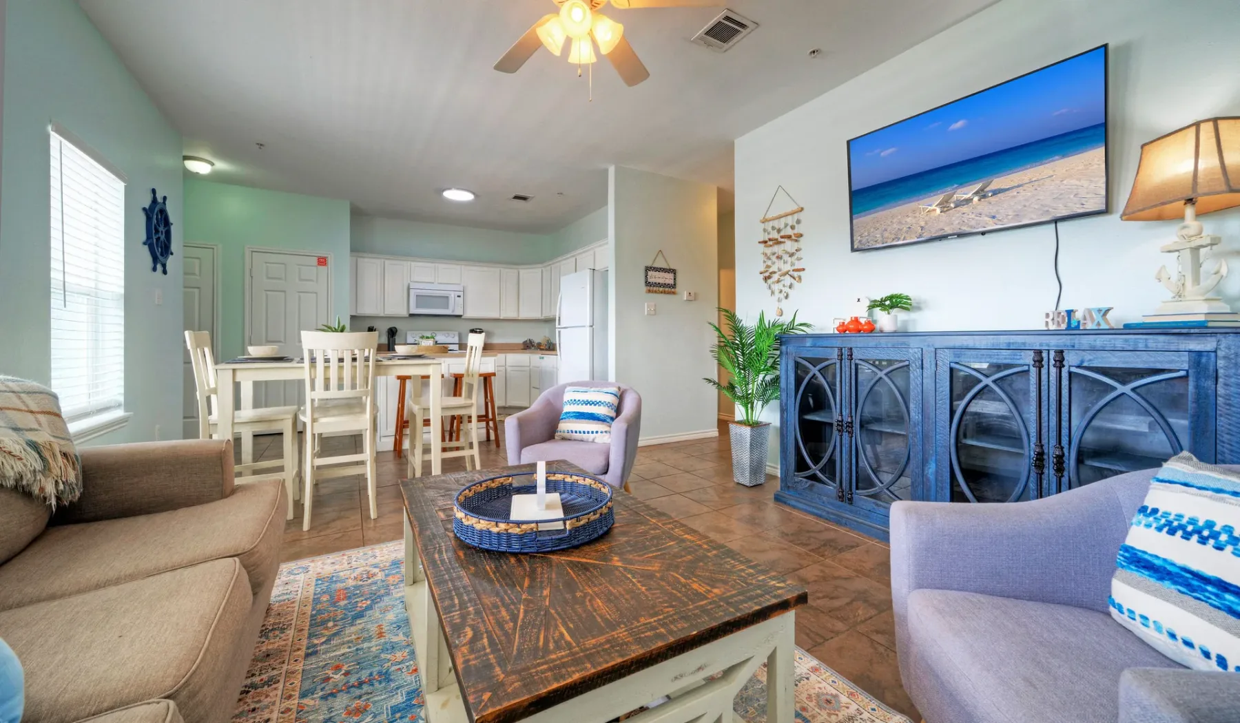 A living room opens onto a dining area and kitchen, with a television above a long cabinet.