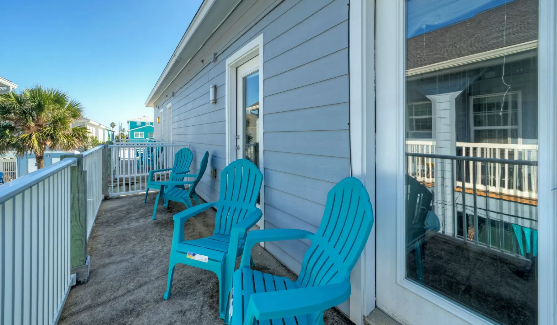 An outdoor balcony with turquoise seating beside a gray-sided building.