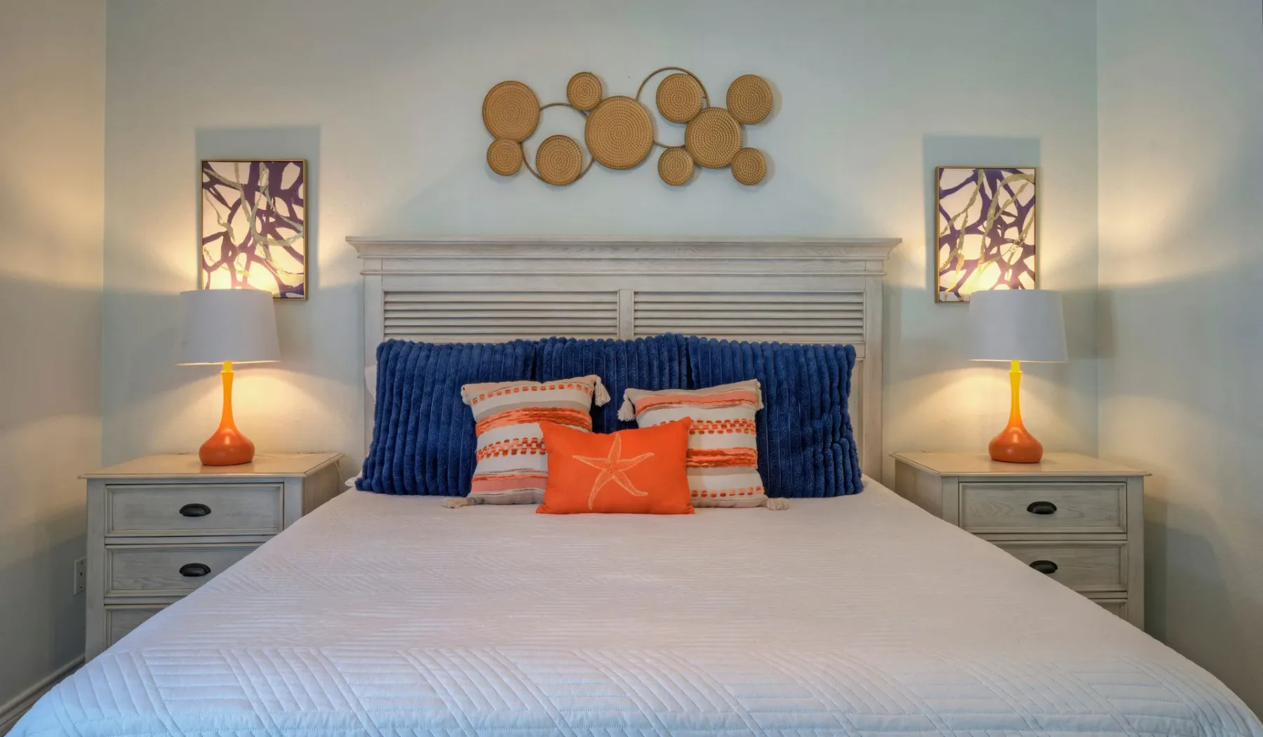 A bedroom with a neatly made bed, colorful pillows, and matching bedside lamps.