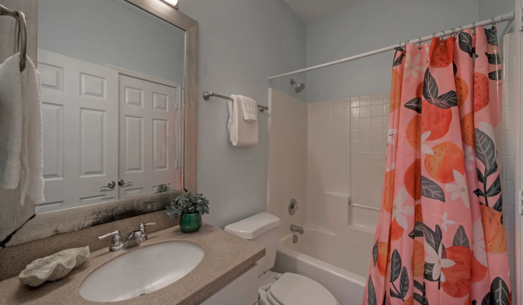 A bathroom vanity with a sink sits beside a bathtub with a colorful shower curtain.