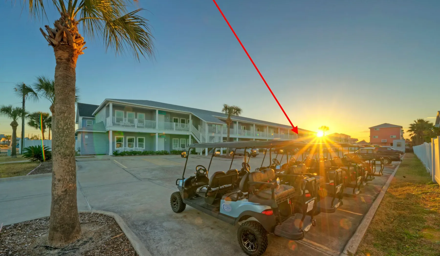 Golf carts are parked beside a two-story building as the sun sets.