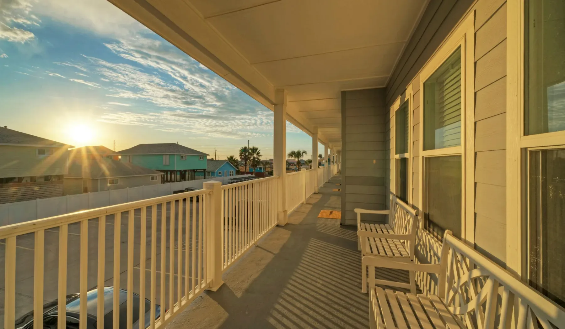 A covered balcony with railings and seating overlooks nearby buildings at sunset.