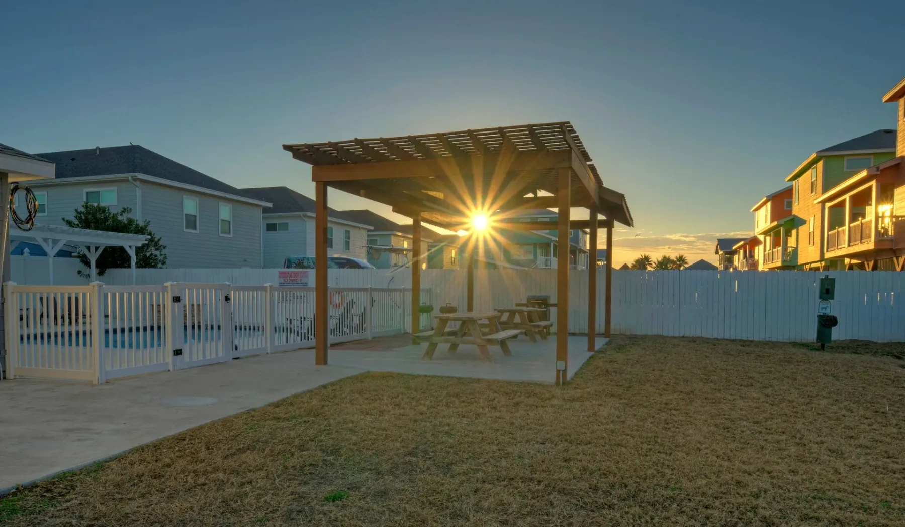 A fenced outdoor courtyard with a pergola and picnic table at sunset.