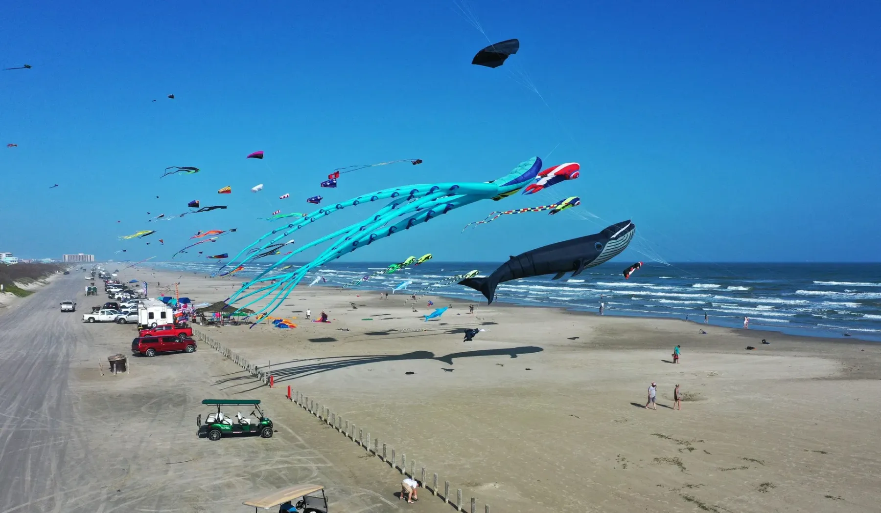 A sandy beach with colorful kites flying above the shoreline.