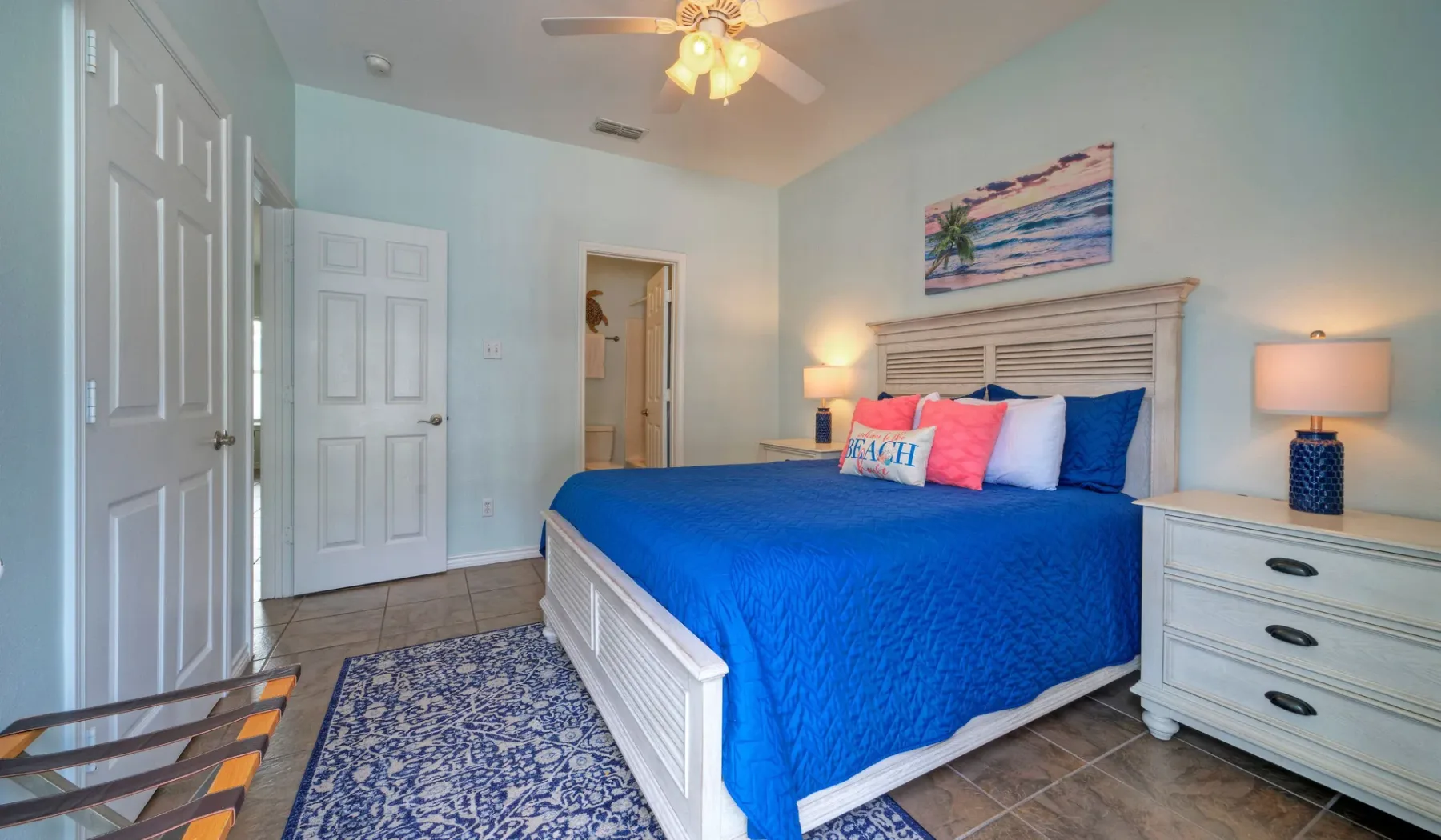 A bedroom with a blue-covered bed, bedside lamps, and a patterned rug.