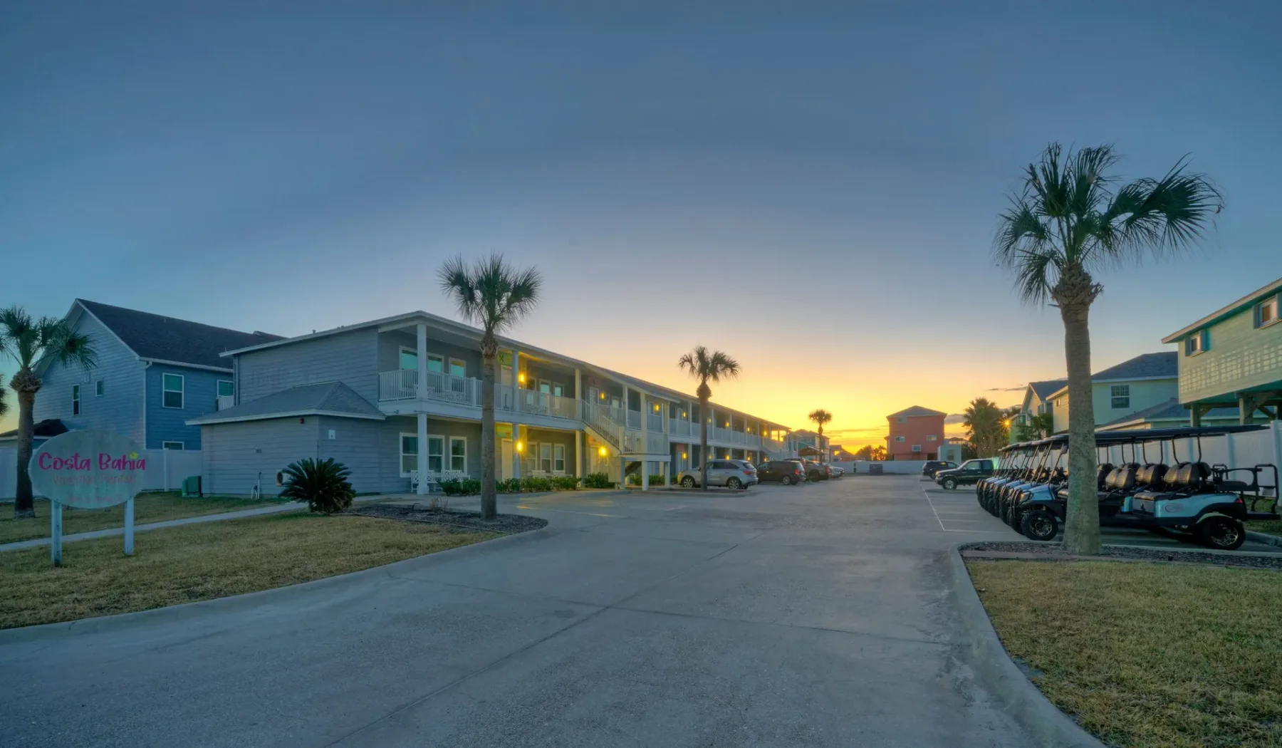 A paved drive runs between low buildings and parked golf carts at dusk.