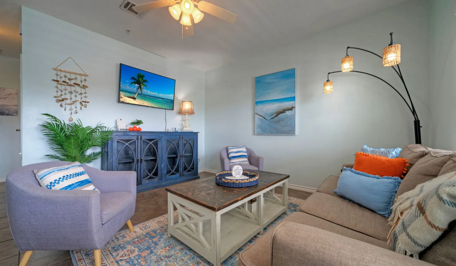 A living room with seating, a coffee table, and colorful coastal artwork.