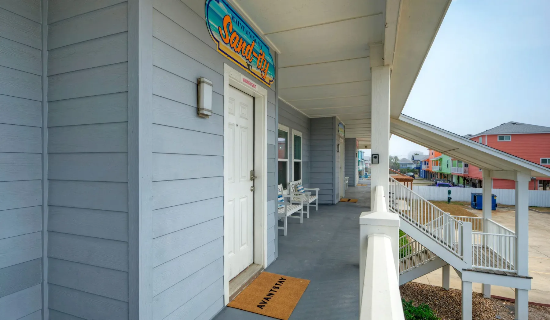 An elevated outdoor walkway runs past a light blue building and white railings.