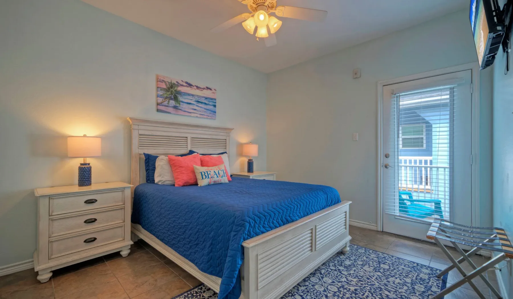 A bedroom with a blue-covered bed, bedside tables, and a glass door to a balcony.
