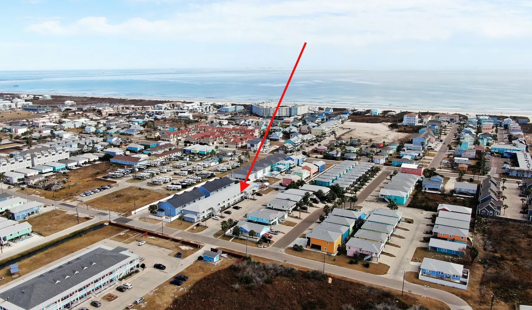 An aerial view of a coastal neighborhood with low-rise buildings and the ocean beyond.