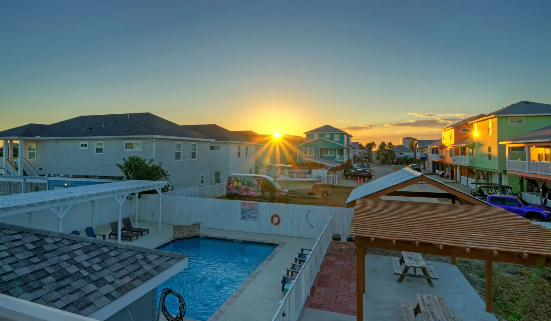 Coastal residential buildings surround an outdoor pool at sunset.