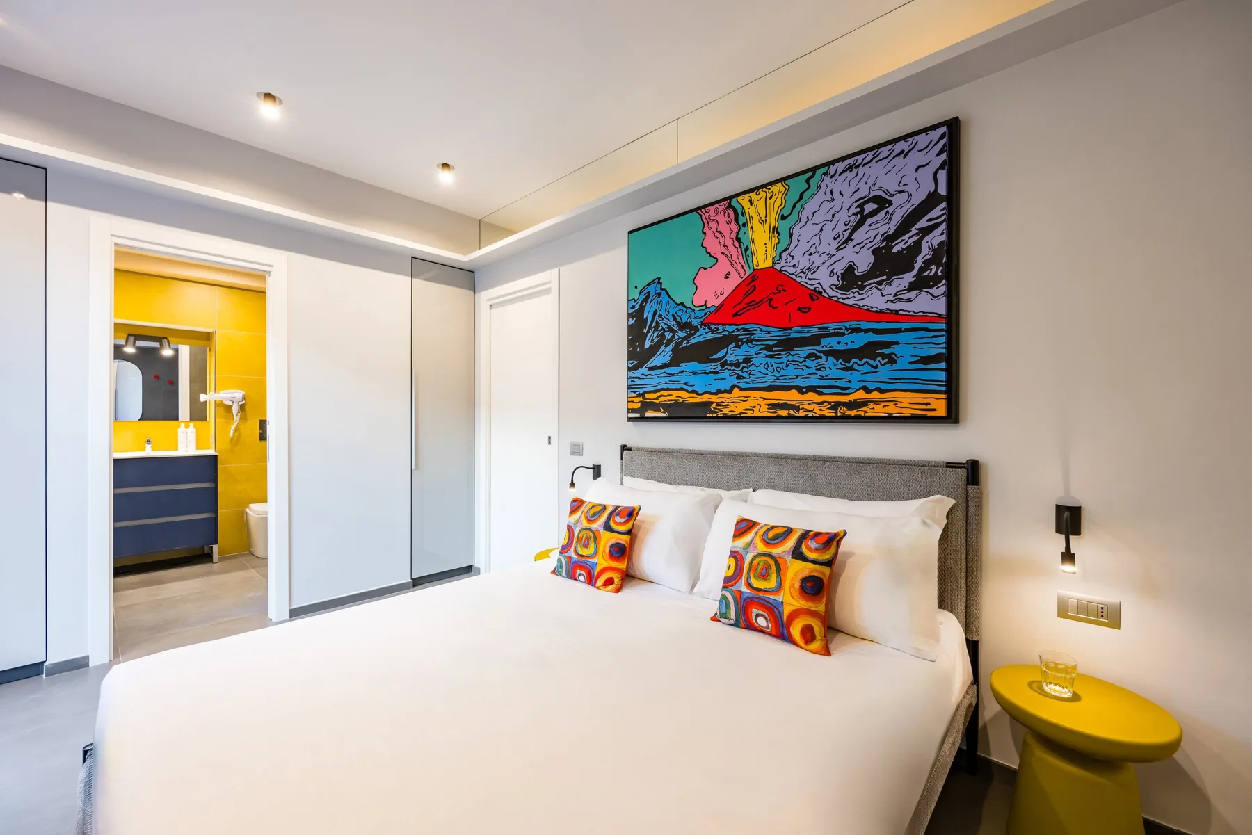 Un dormitorio luminoso con una cama grande y una obra colorida sobre el cabecero.