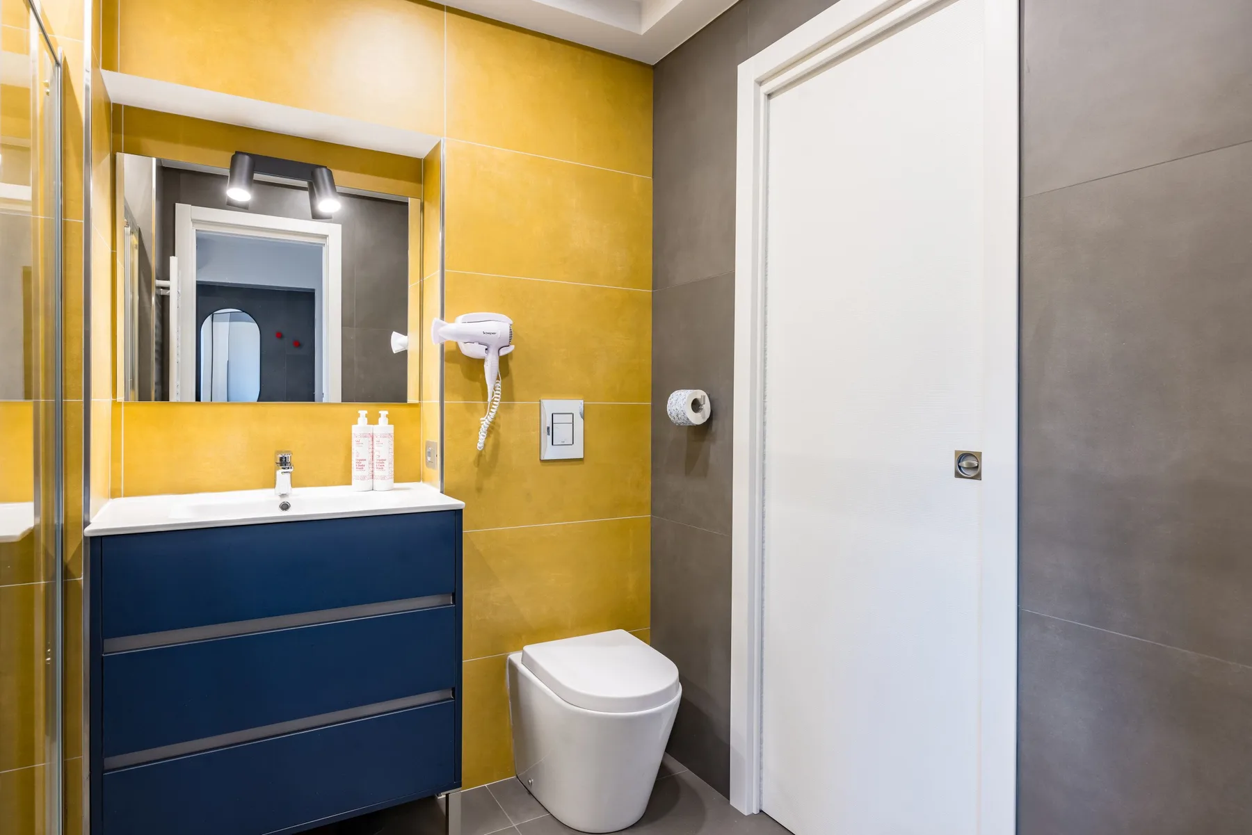 Un baño moderno con un mueble oscuro, un espejo grande y un inodoro blanco.
