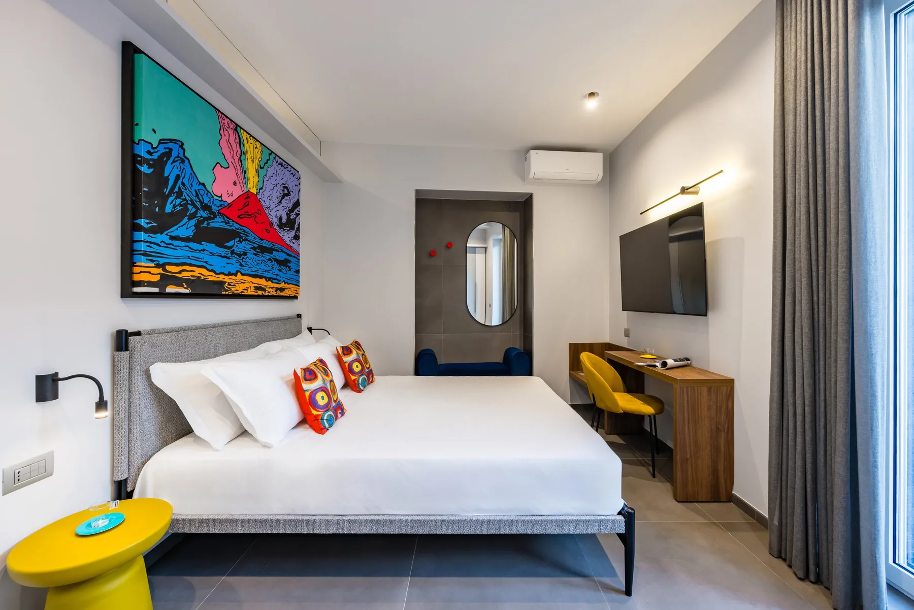 Un dormitorio con una cama bien tendida, arte colorido en la pared y un televisor.
