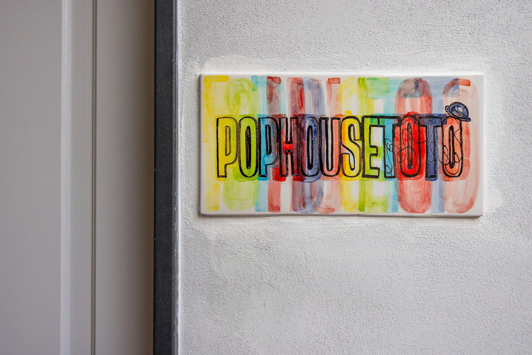 Un letrero de arte pop colorido cuelga en una pared clara junto a una puerta.