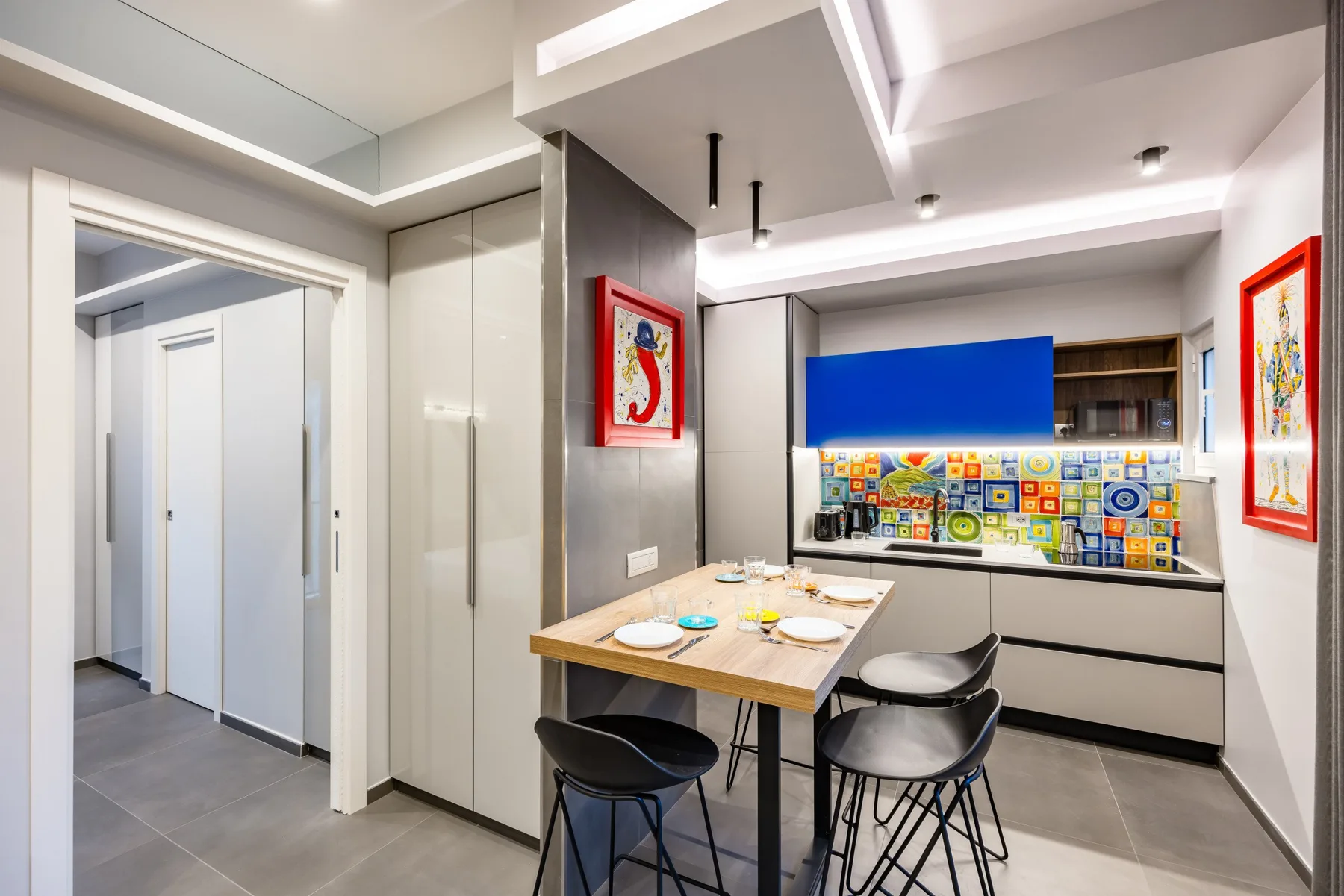 Una cocina luminosa con zona de comedor, mesa, taburetes y un salpicadero colorido.