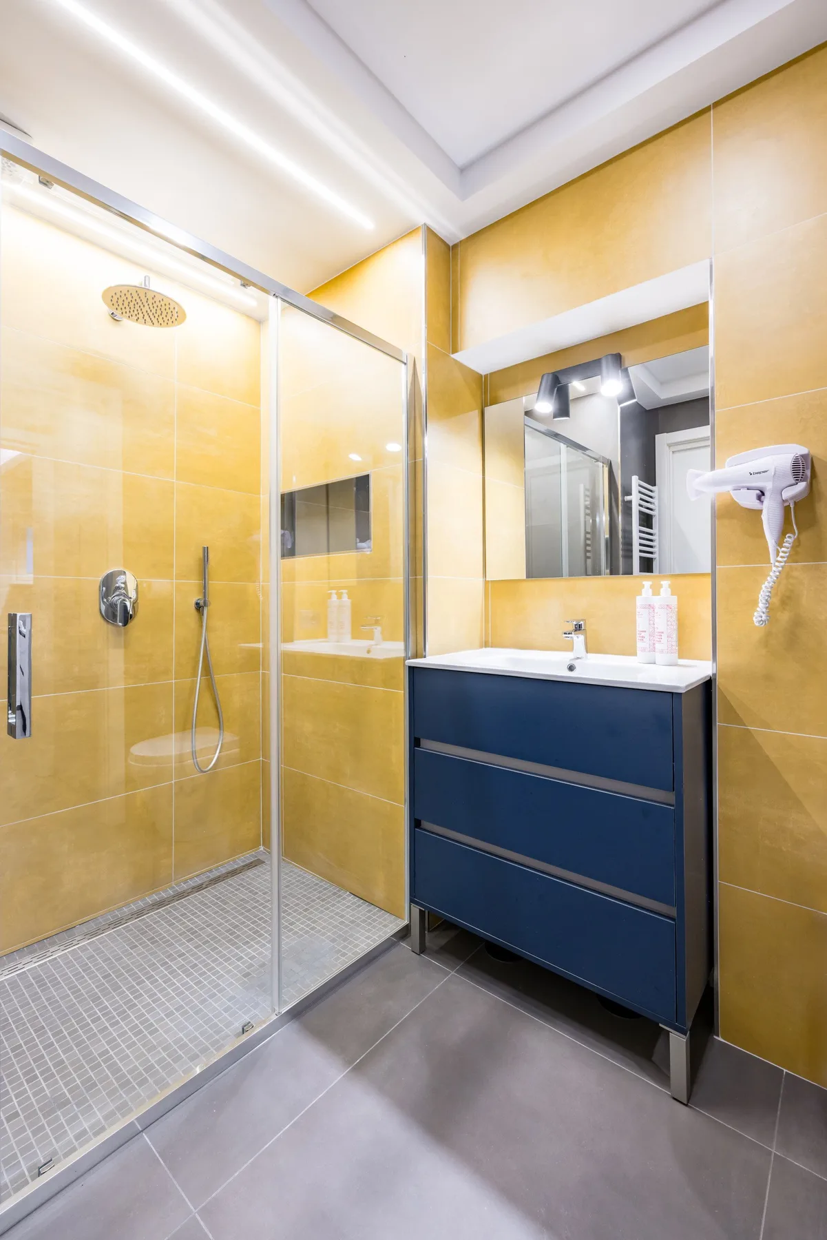 Un baño moderno con una ducha de vidrio y un mueble azul.