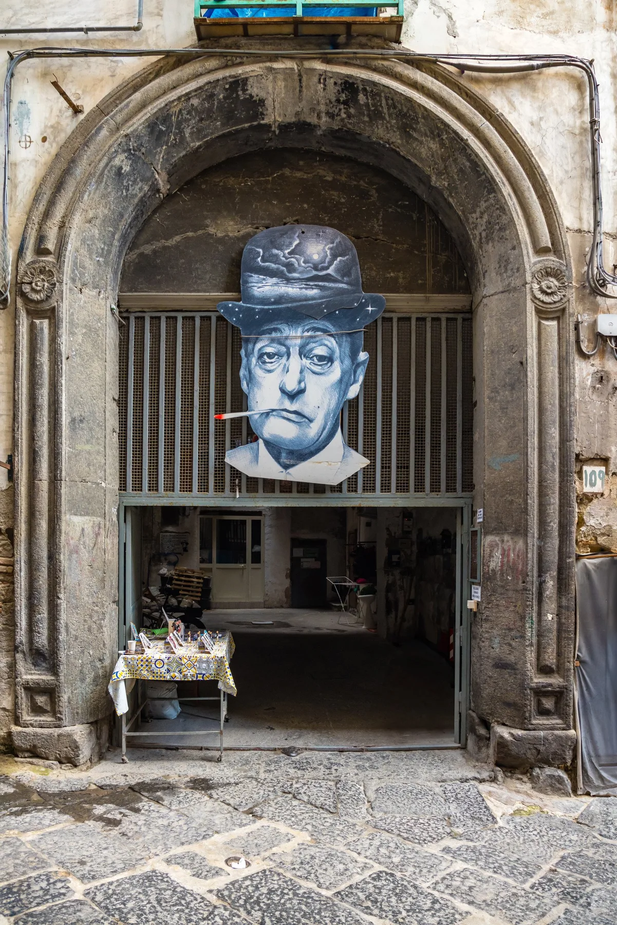 Un arco de piedra ornamentado enmarca una entrada con rejas y un retrato pintado encima.