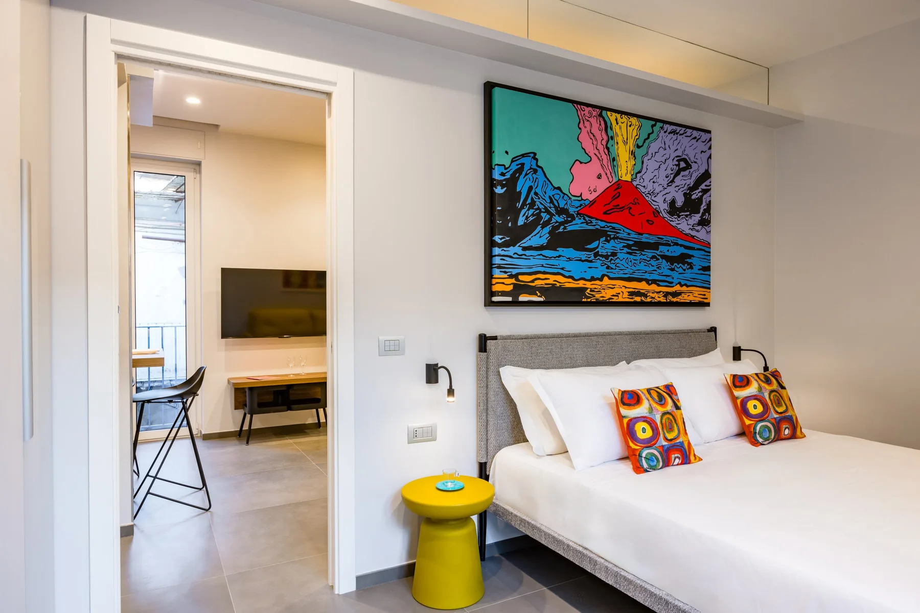 Un dormitorio con una cama bajo una pantalla de colores montada en la pared.