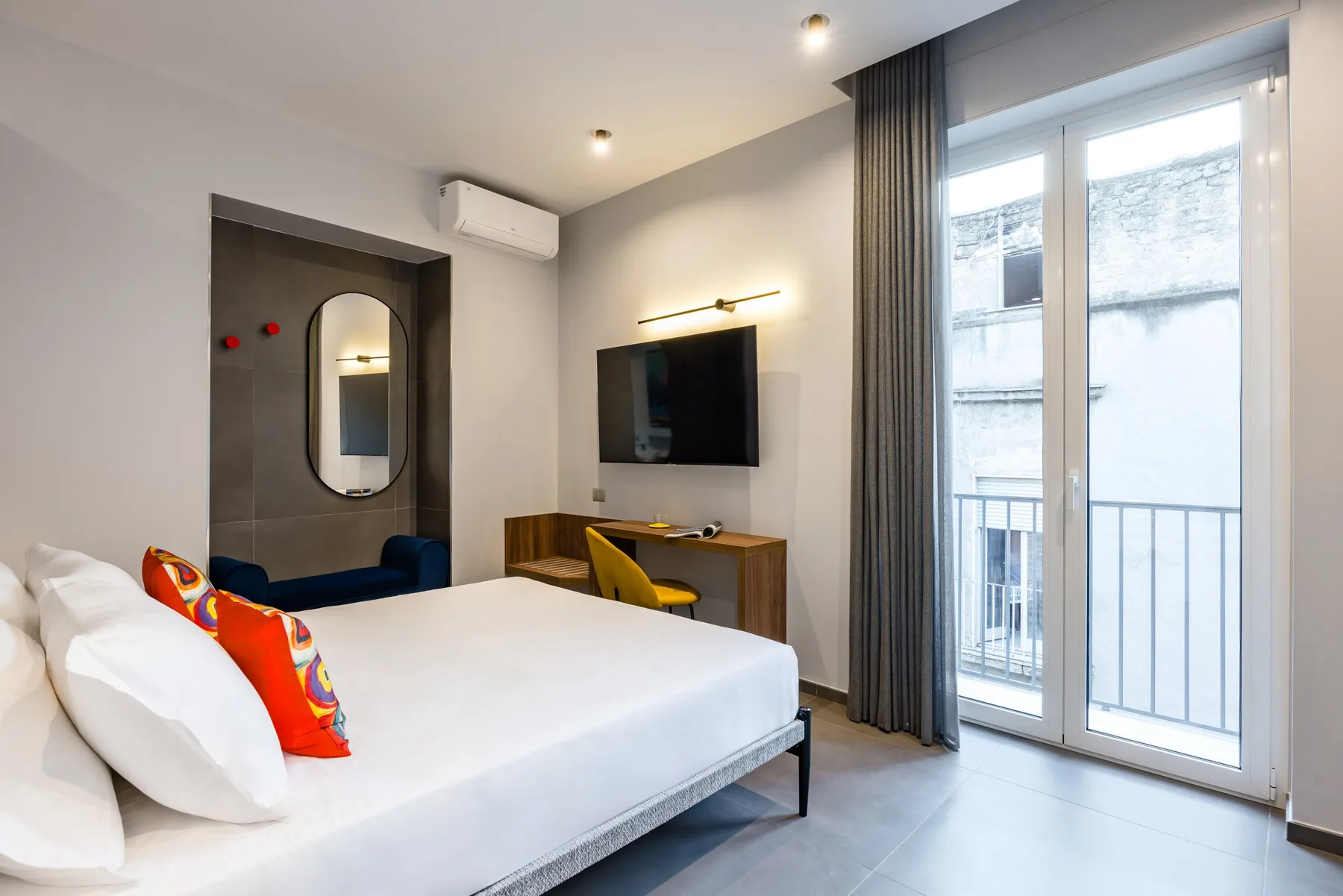 Dormitorio con una cama, un televisor en la pared y puertas acristaladas al balcón.
