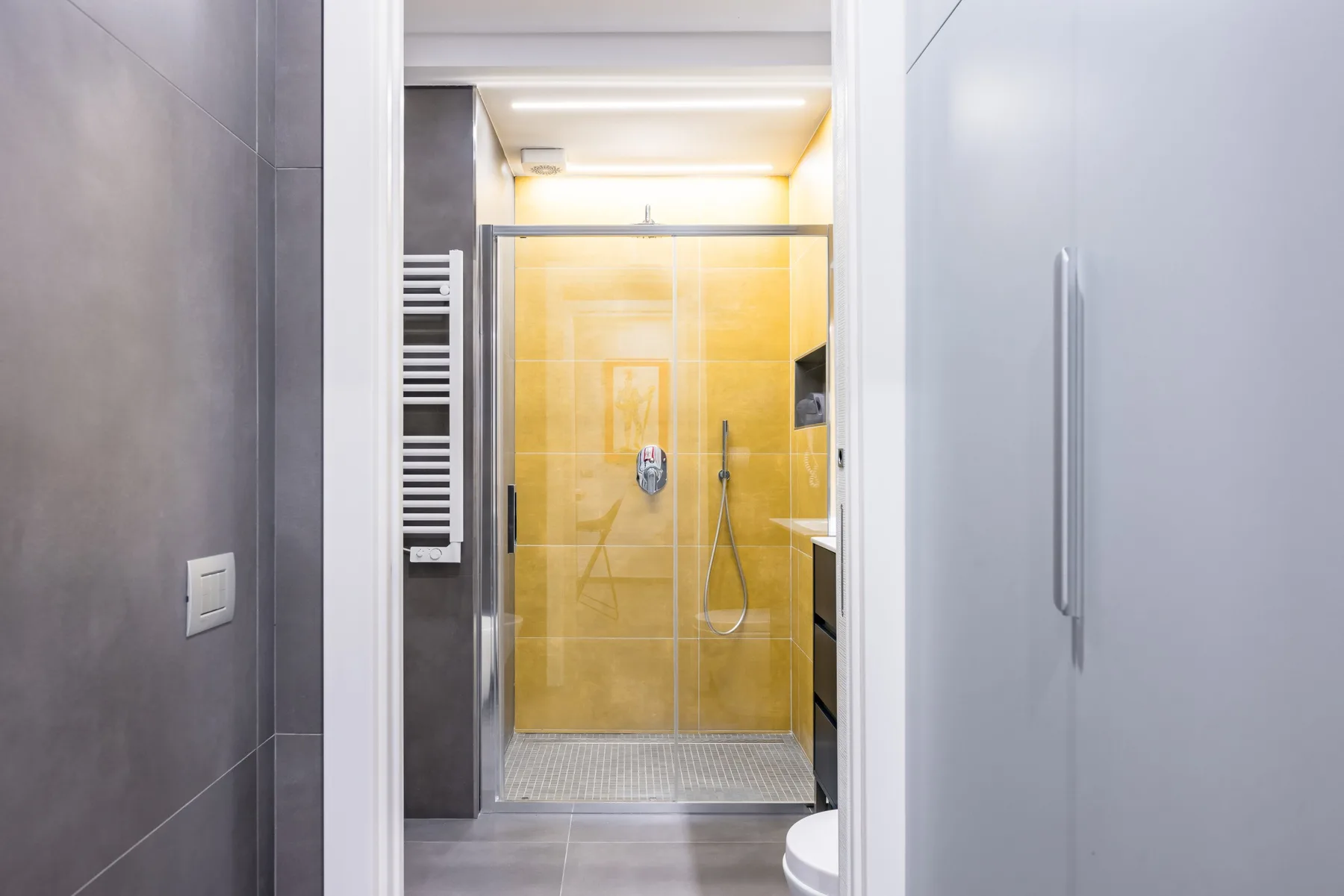 Una ducha de baño con paneles de vidrio y azulejos amarillos.