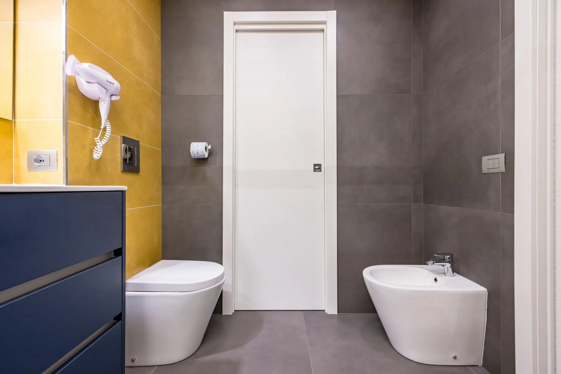 Un baño moderno con lavabo, inodoro y secador de pelo montado en la pared.
