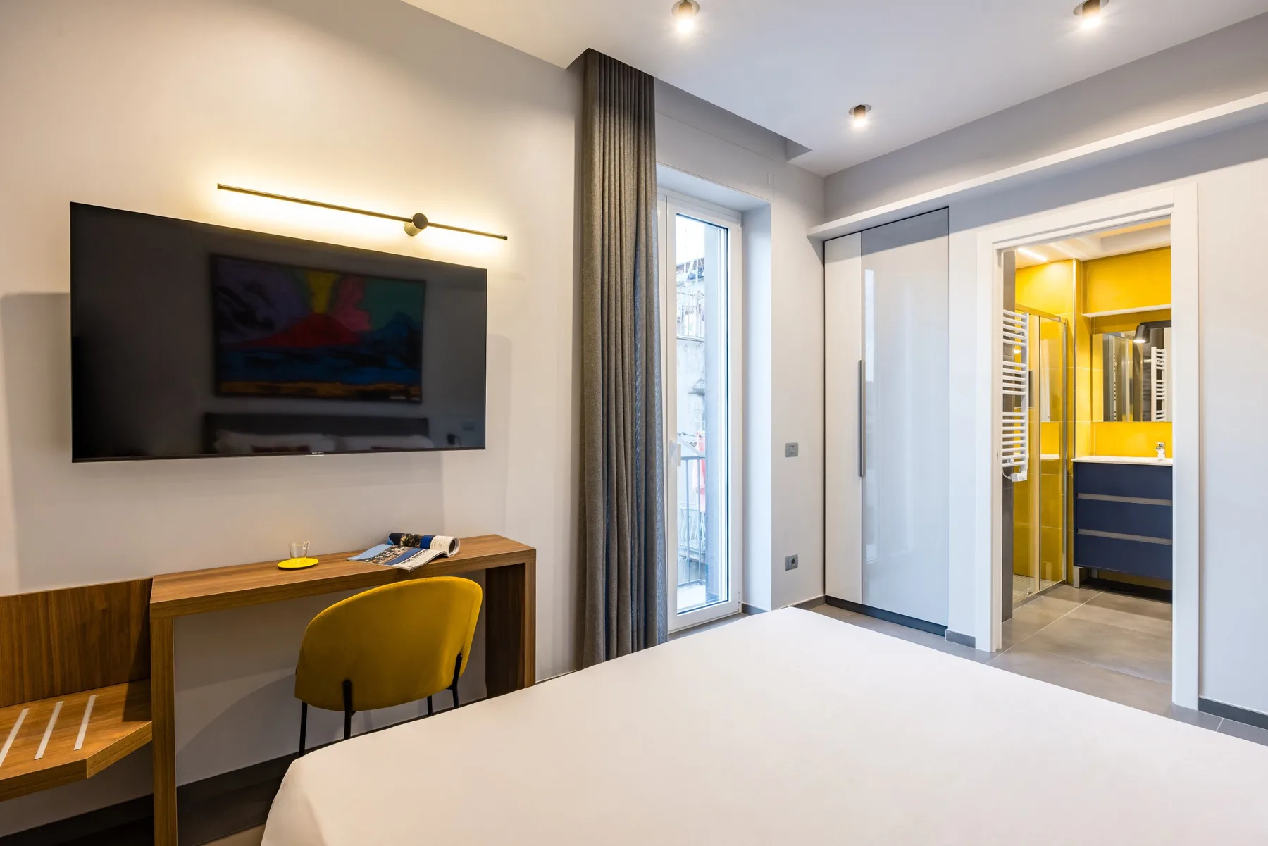 Un dormitorio moderno con cama, televisor en la pared y escritorio.