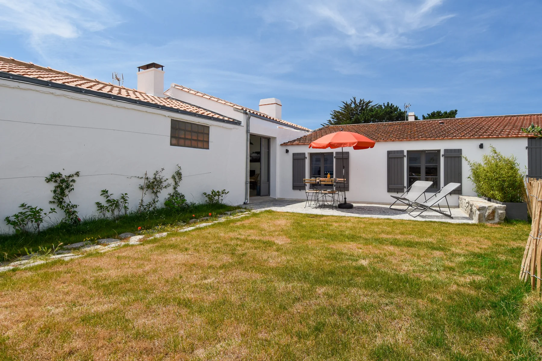 A sunny courtyard with a lawn, outdoor seating, and an umbrella.