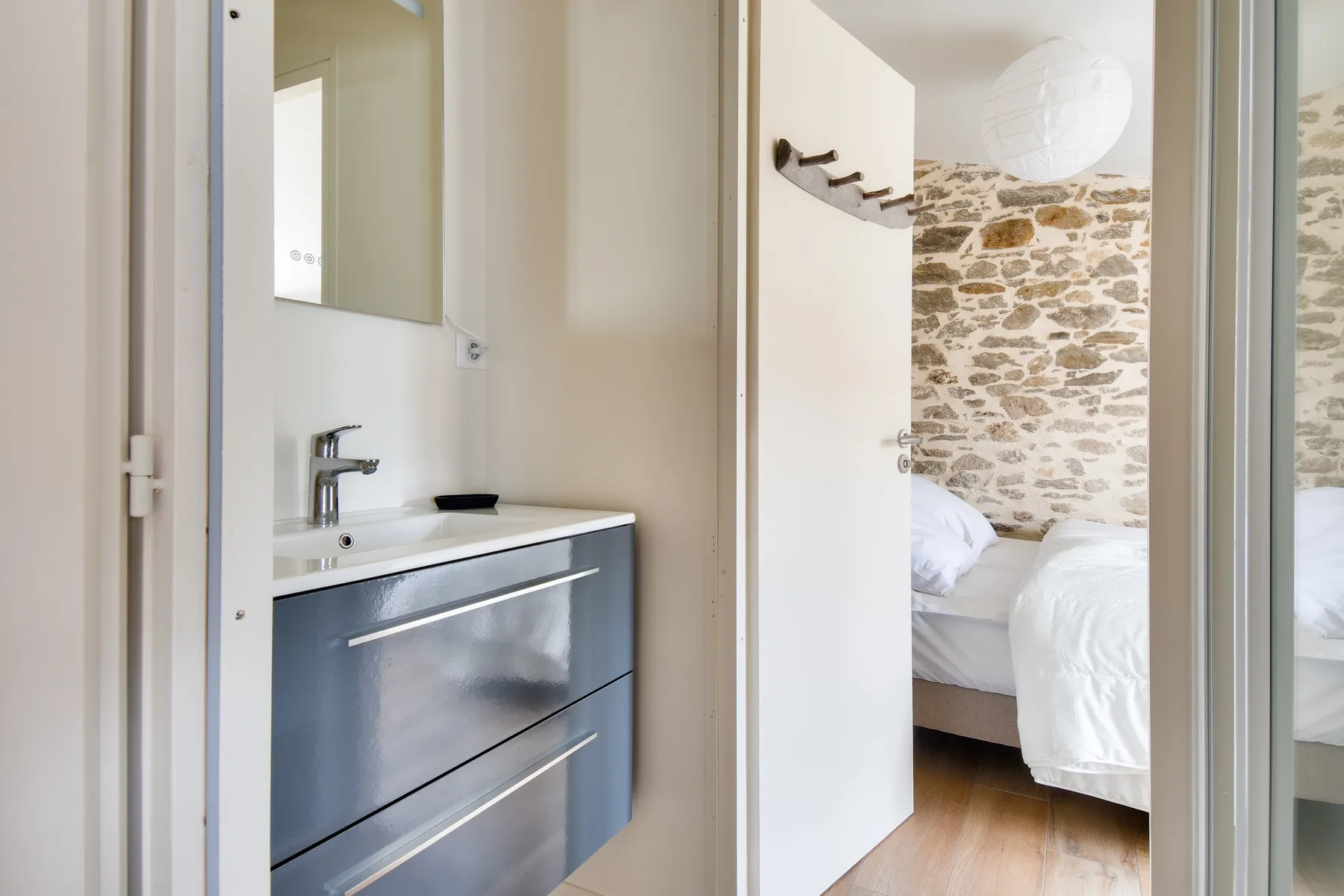 A bathroom vanity opens onto a bedroom with a stone accent wall.