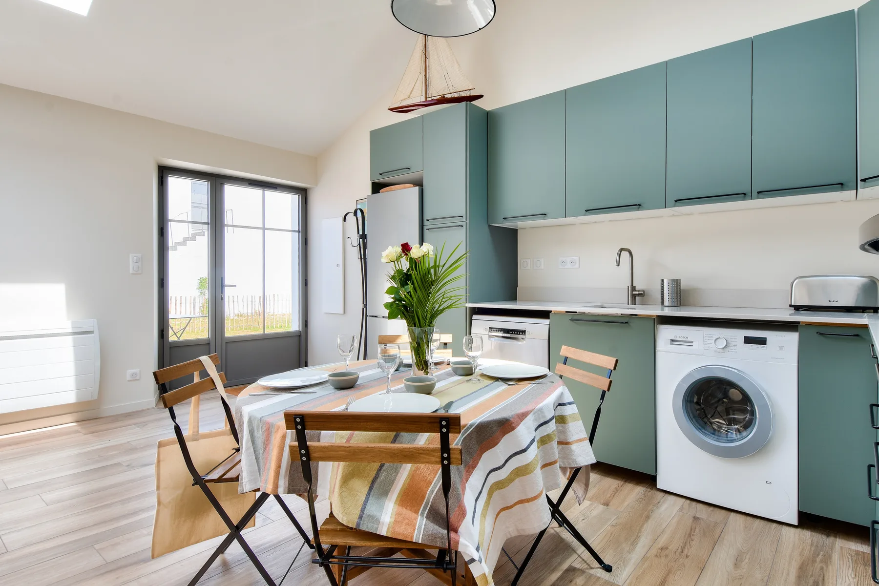 A dining area beside a kitchen with teal cabinets and a table.