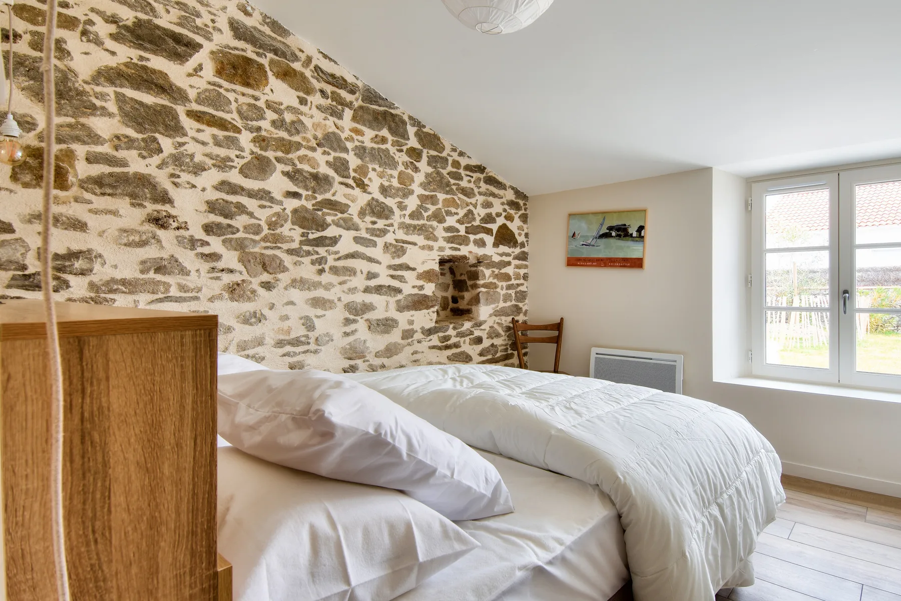 A bedroom with a bed beside a stone wall and a bright window.