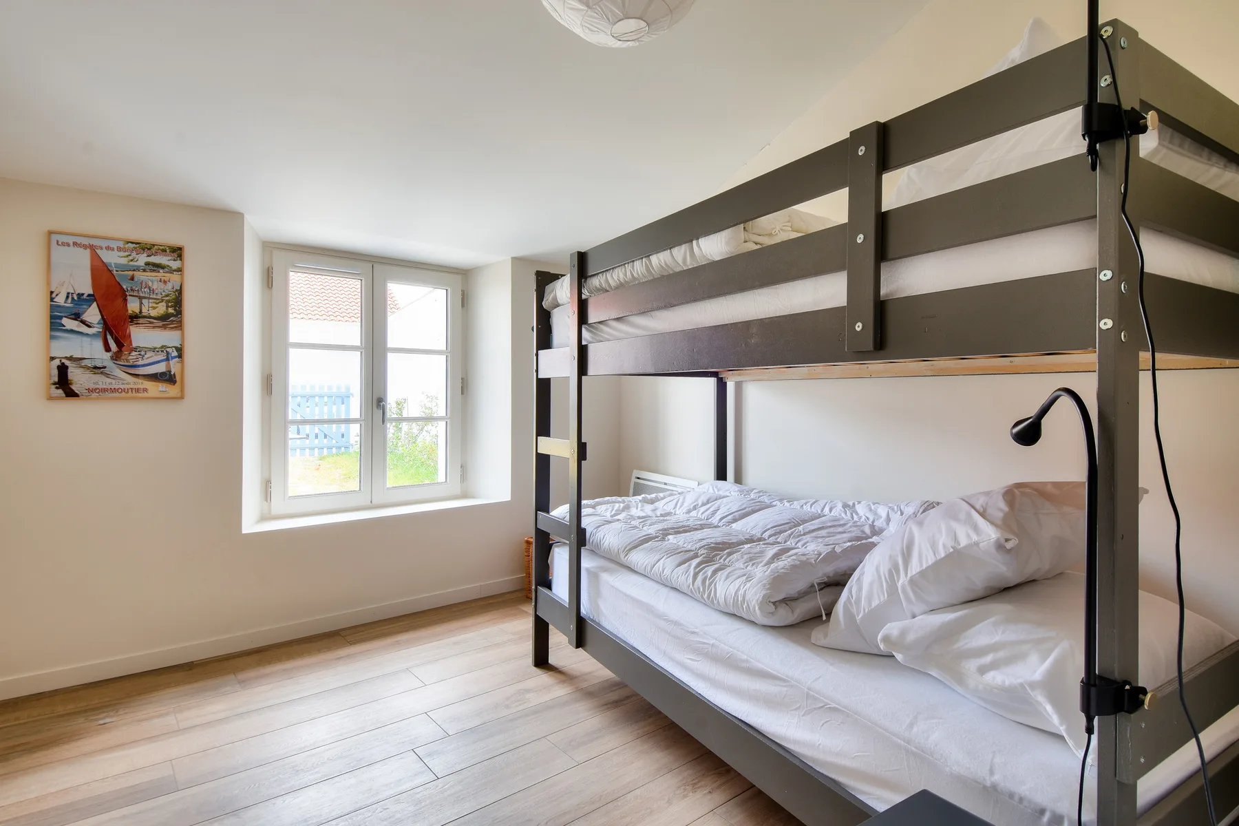 A bright bedroom with a dark bunk bed beside a window.