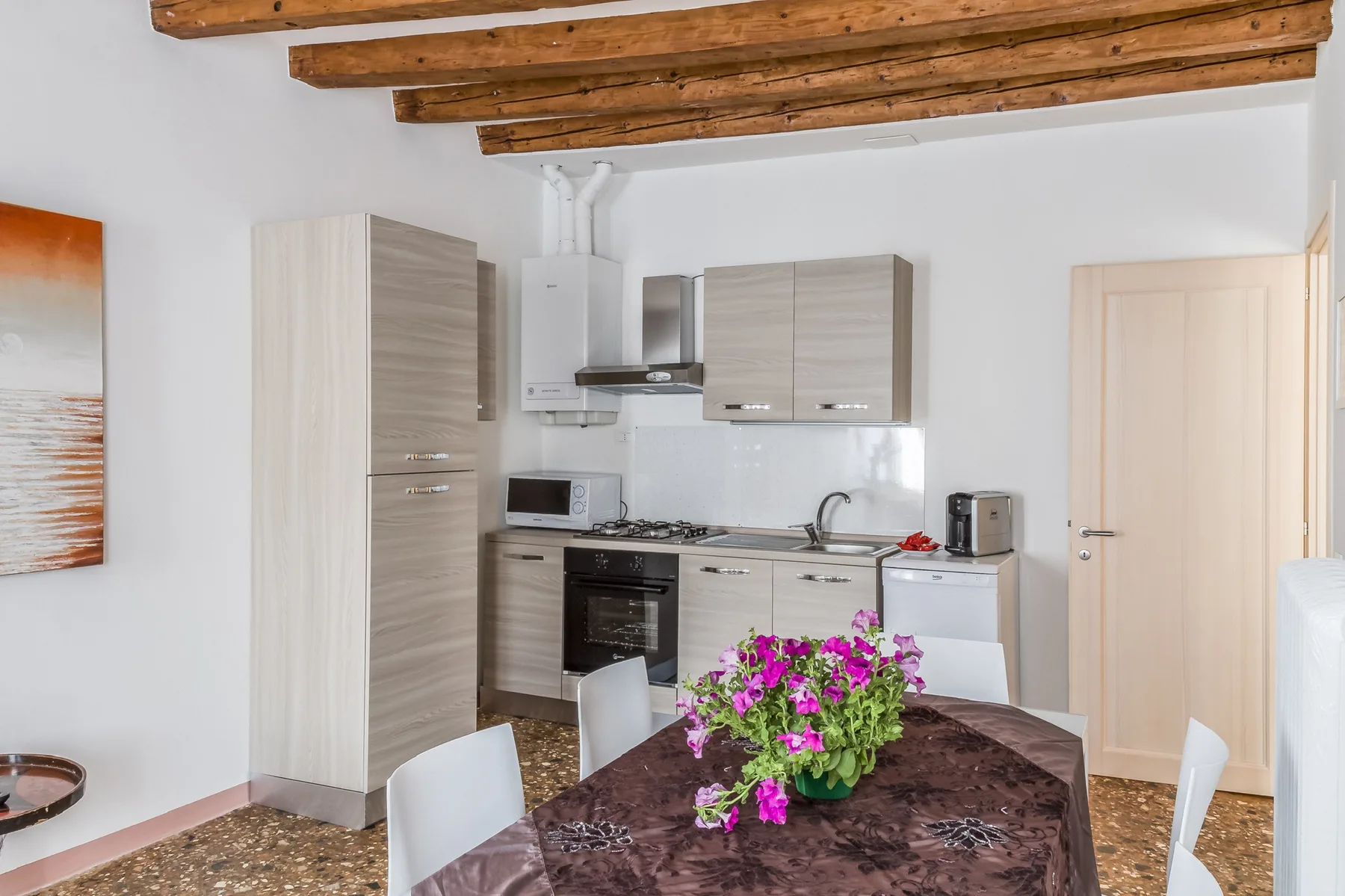 Una cocina y comedor con gabinetes claros y flores sobre la mesa.