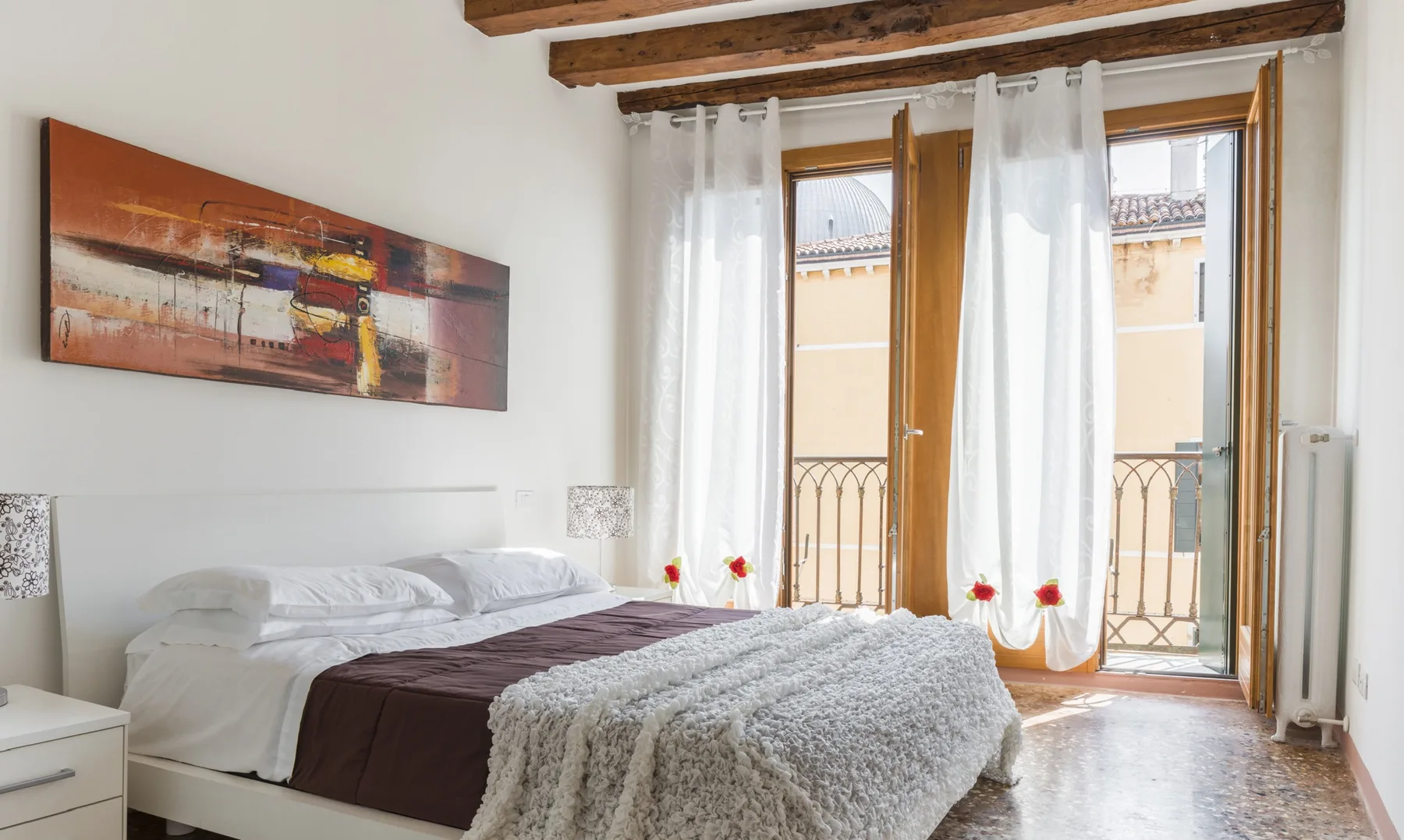 A bright bedroom with a bed beside tall windows and sheer curtains.