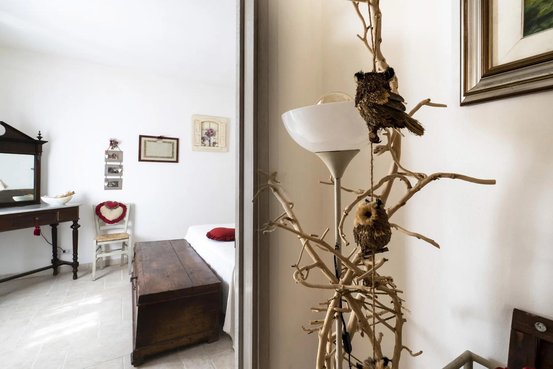 Un dormitorio con una cama de madera oscura y un arreglo decorativo de ramas junto a una lámpara de pie.