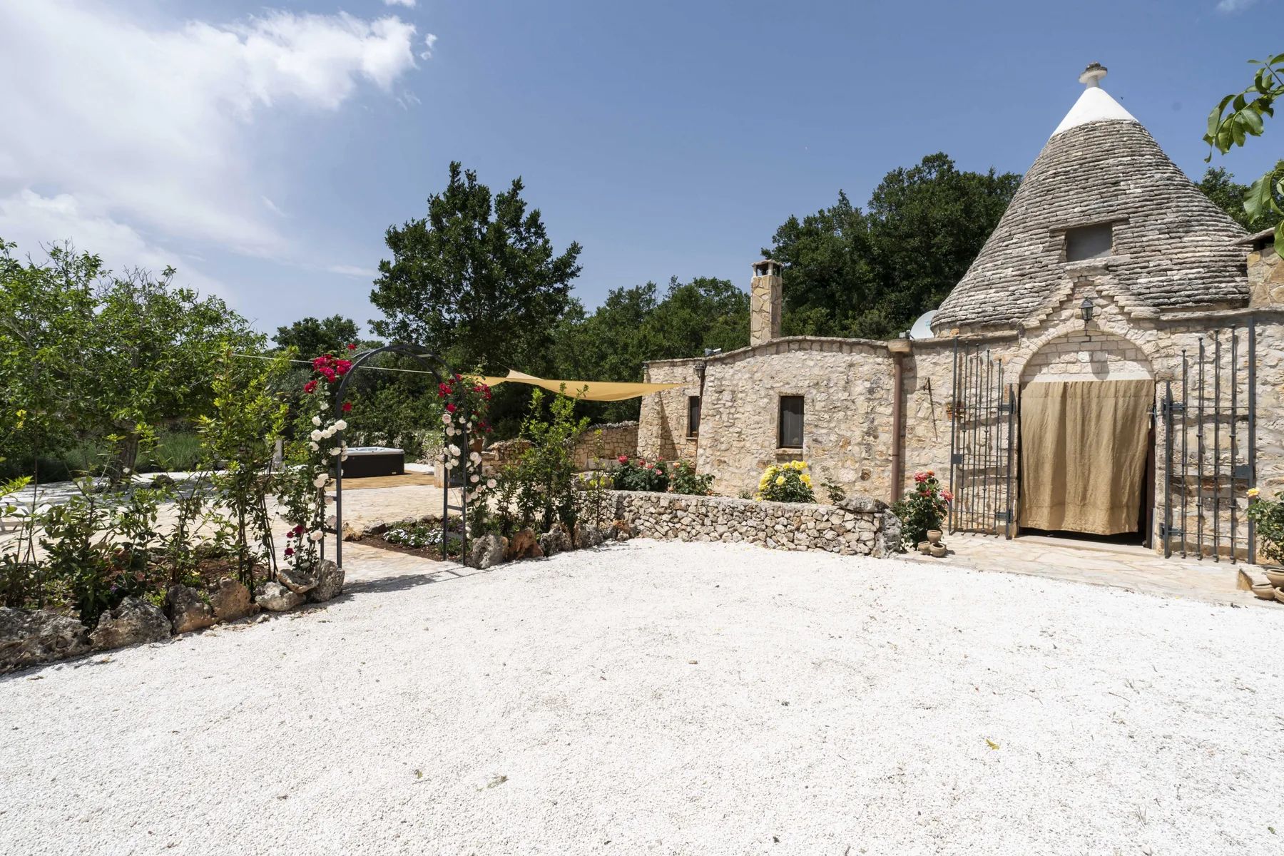 Un edificio de piedra con techo cónico se alza junto a un patio de grava y un jardín.