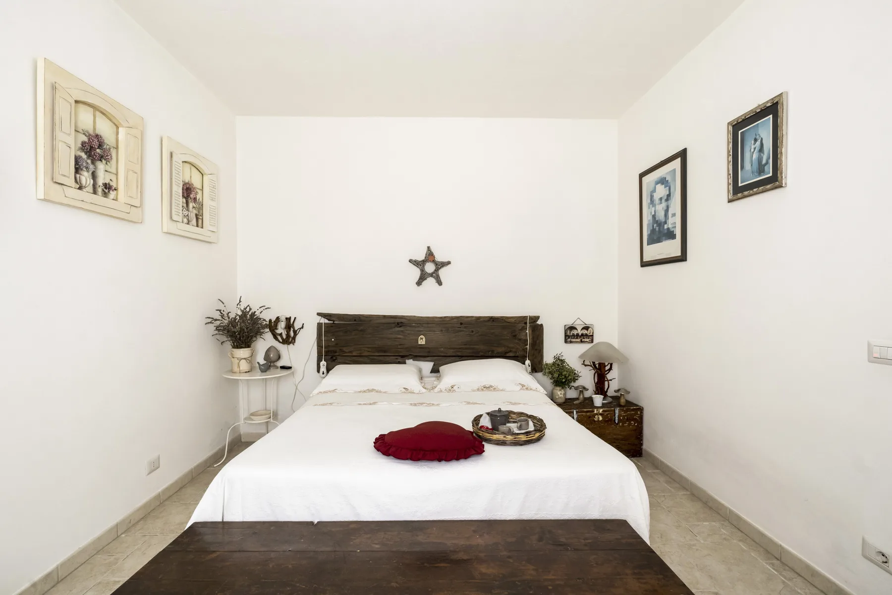 Un dormitorio luminoso con una cama tendida y cuadros en las paredes.