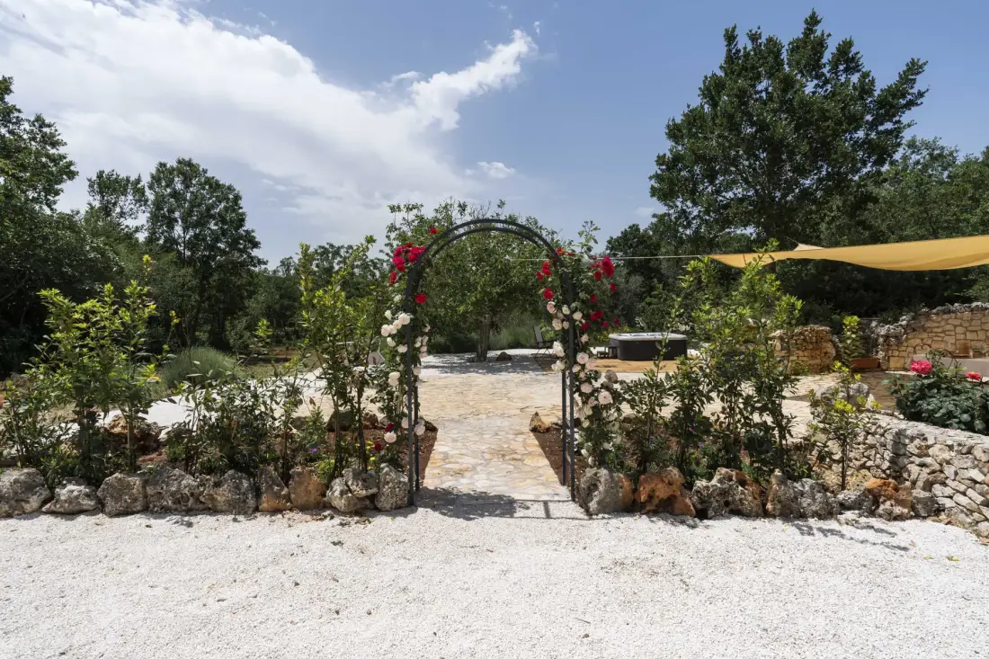 La entrada de un jardín, con un arco cubierto de flores, da a un sendero de piedra.