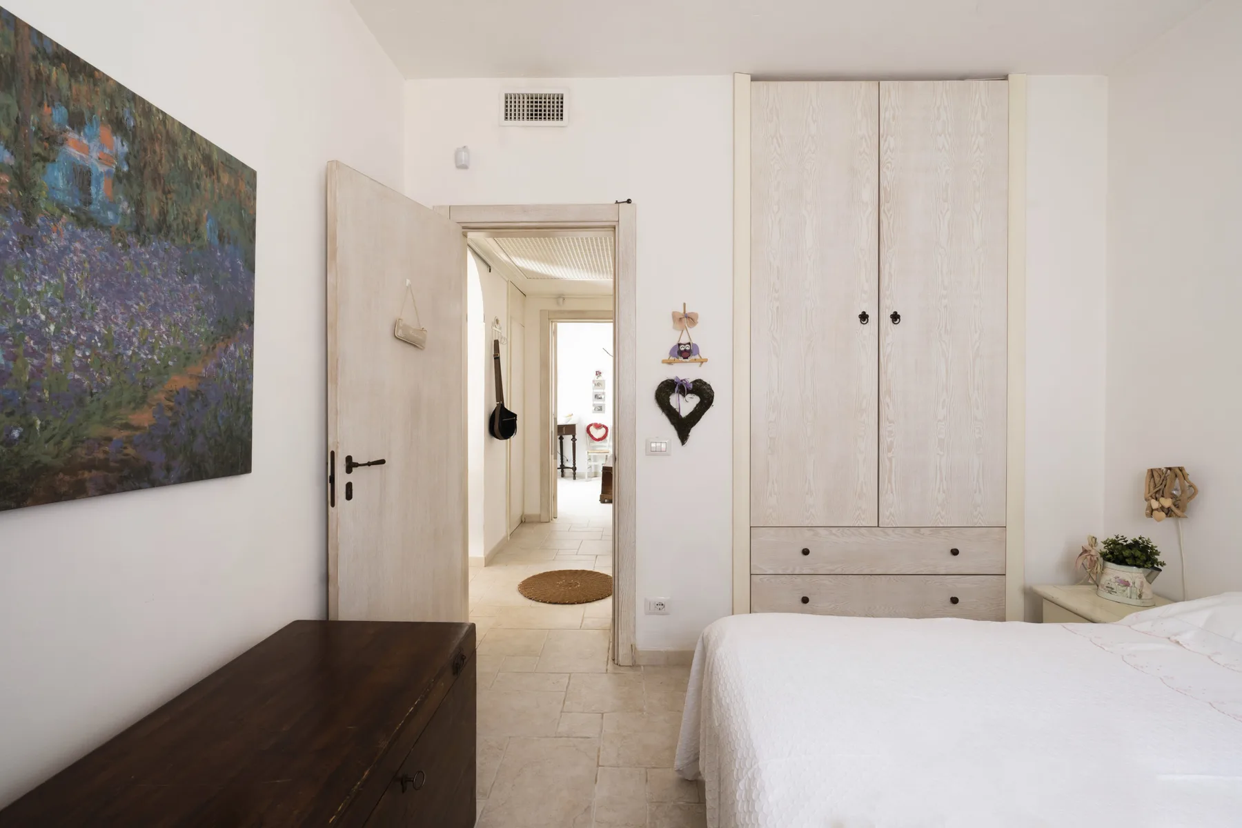 Un dormitorio con una cama blanca, una cómoda oscura y una puerta abierta.