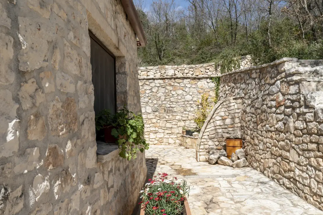 Un patio de piedra con un sendero pavimentado y plantas con flores junto al edificio.
