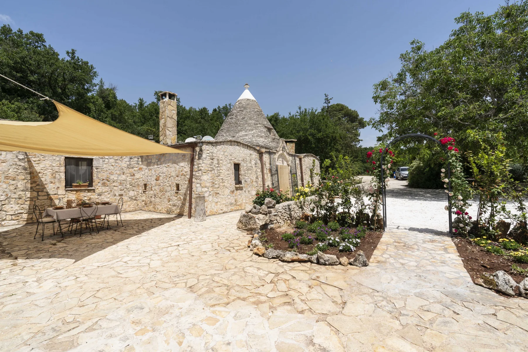 Un patio de piedra con un edificio de techo cónico, asientos a la sombra y jardines.