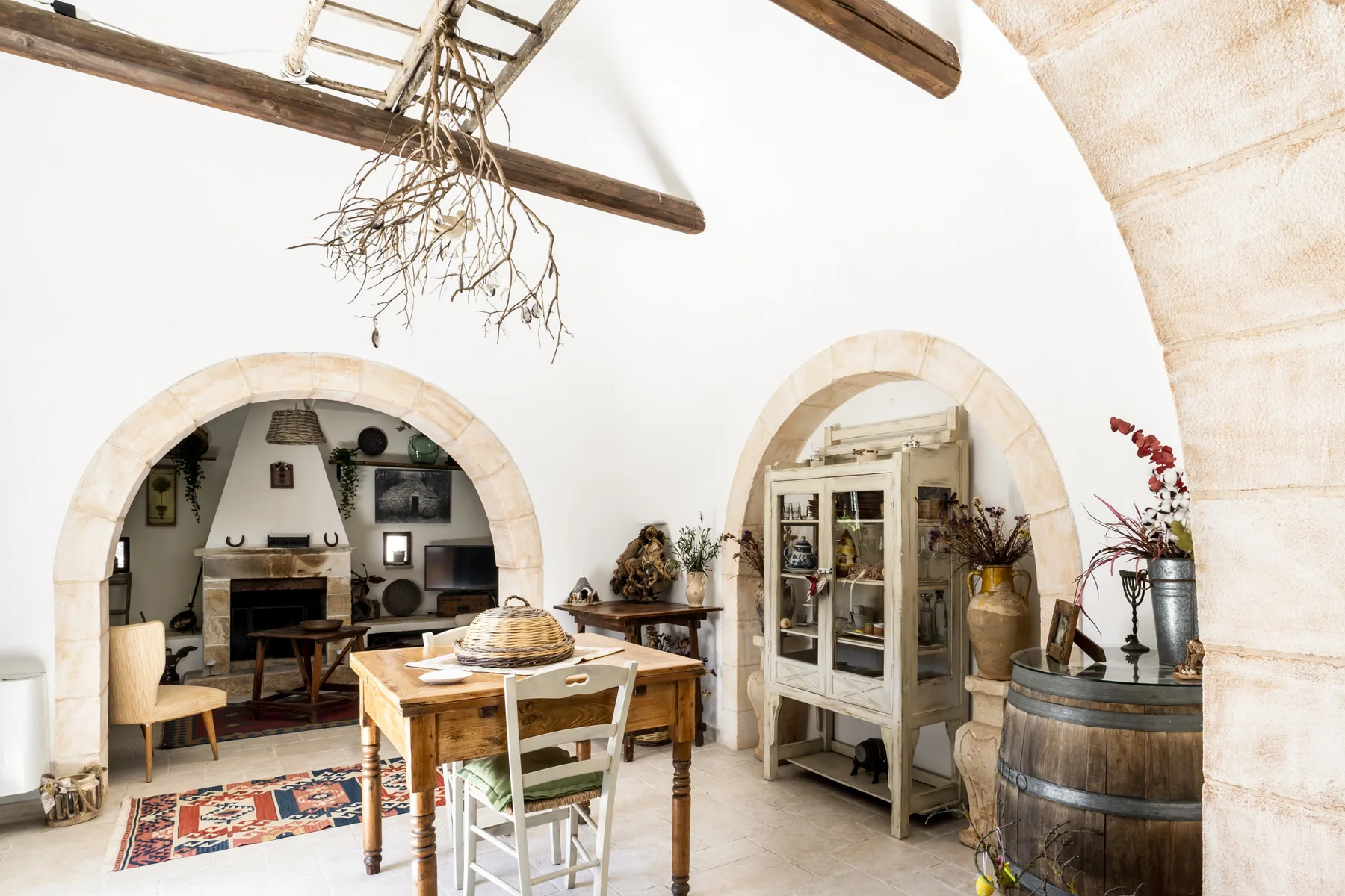 Interior rústico con arcos, una mesa de madera y un armario con puertas de vidrio.