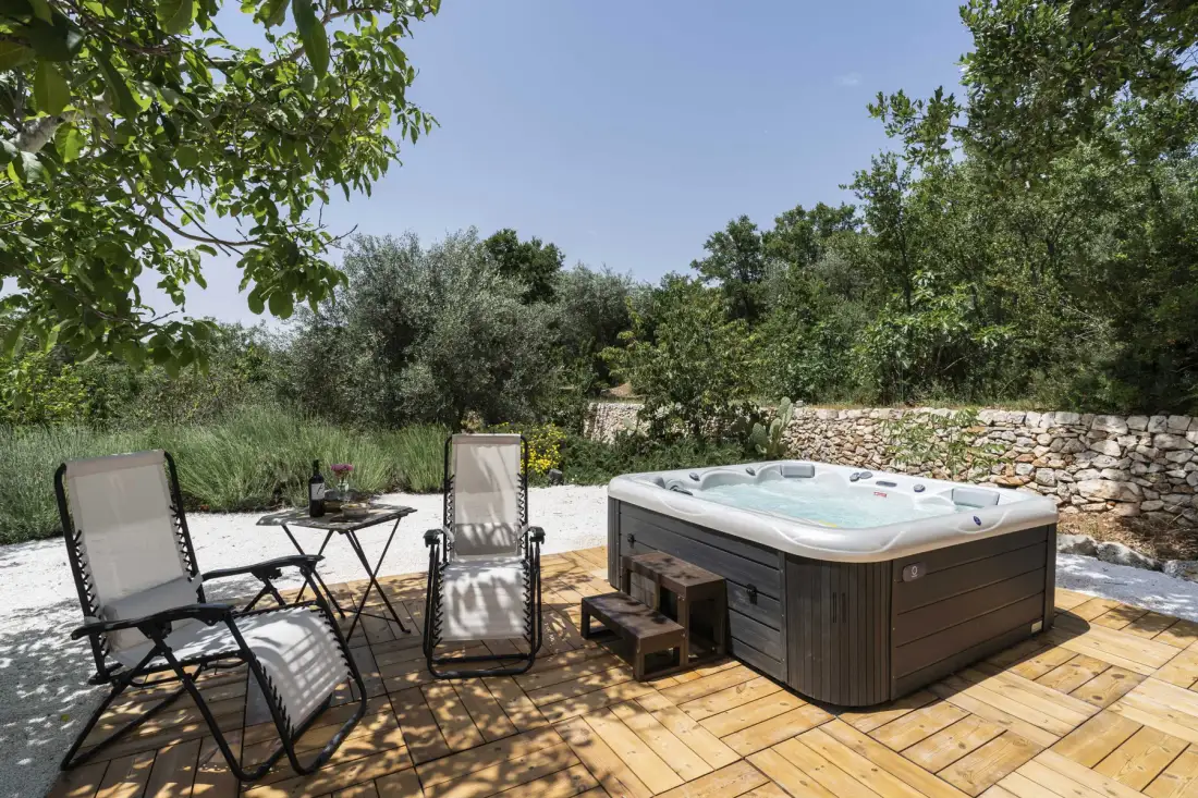 Un patio al aire libre tiene una bañera de hidromasaje y asientos junto a un muro de piedra.