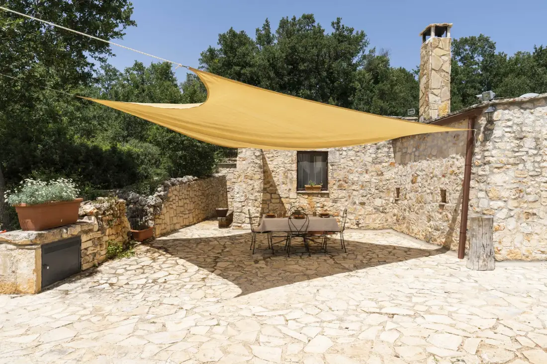 Un patio de piedra con una mesa de comedor está bajo una gran cubierta de sombra.