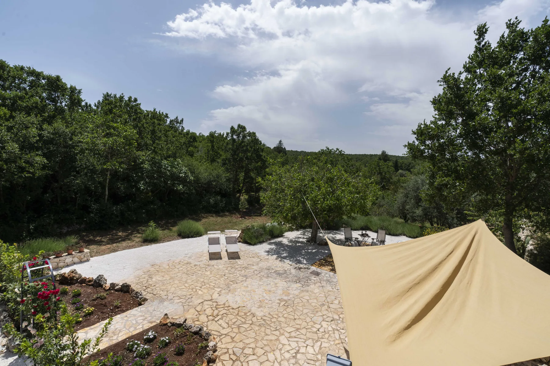 Un patio de piedra con asientos al aire libre da a un jardín arbolado.