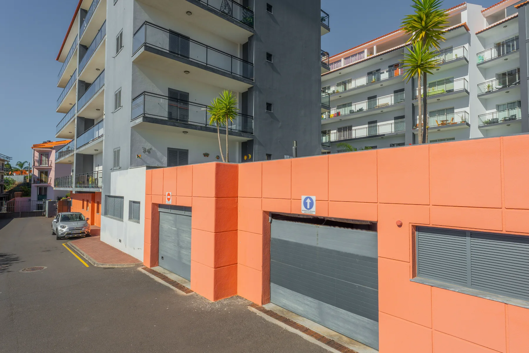 Edificios de apartamentos con balcones se alzan sobre una fachada naranja de garaje junto a una calle.