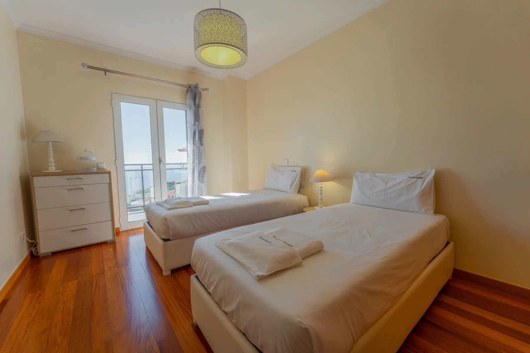 Dormitorio con dos camas, toallas dobladas y puertas de cristal que dan a un balcón.