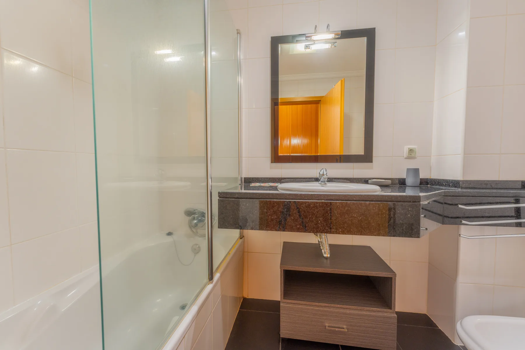 Un baño alicatado con una ducha de vidrio, lavabo y espejo de pared.