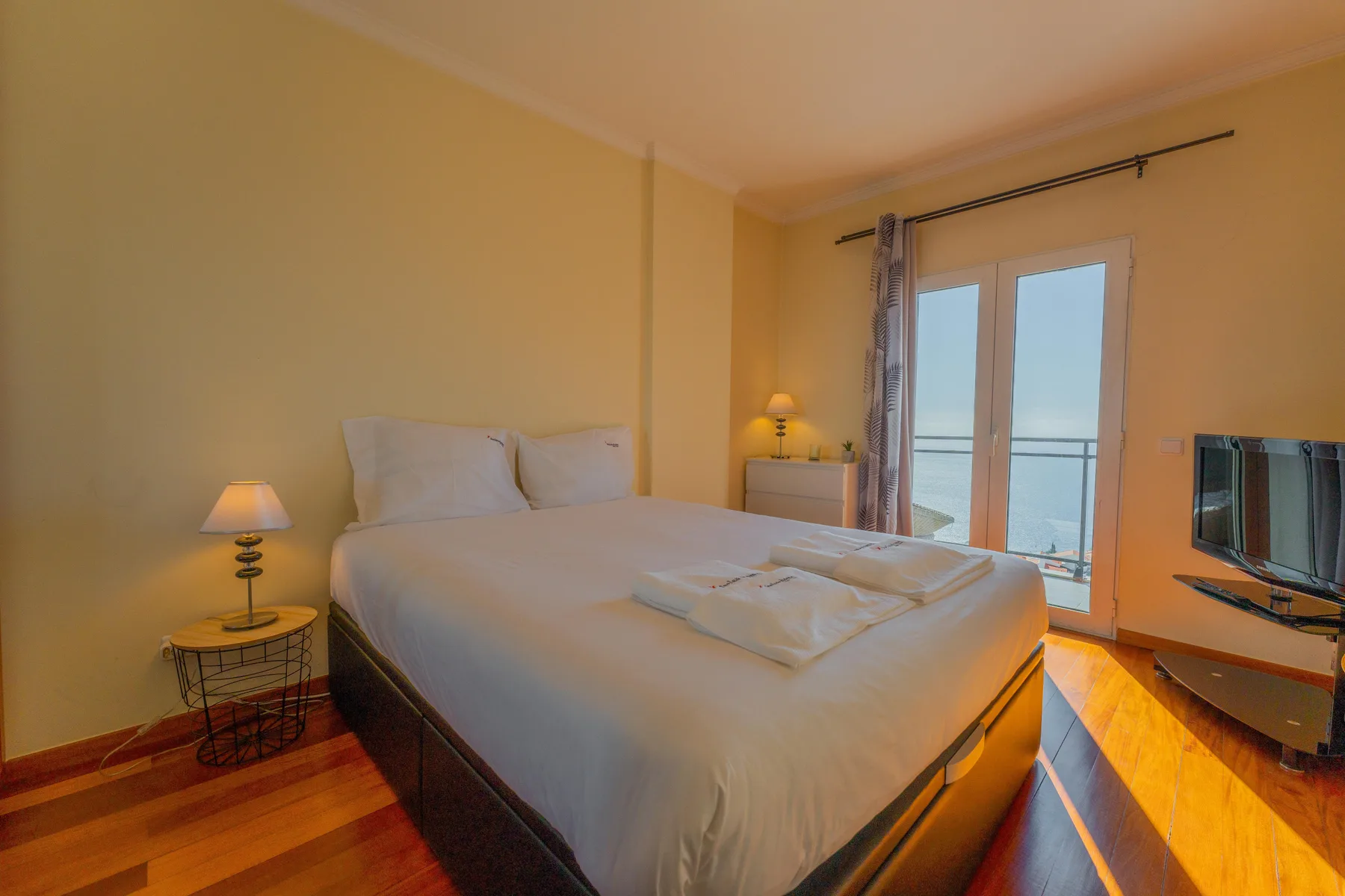 Un dormitorio con una cama grande, mesitas de noche y puertas de vidrio que dan a un balcón.